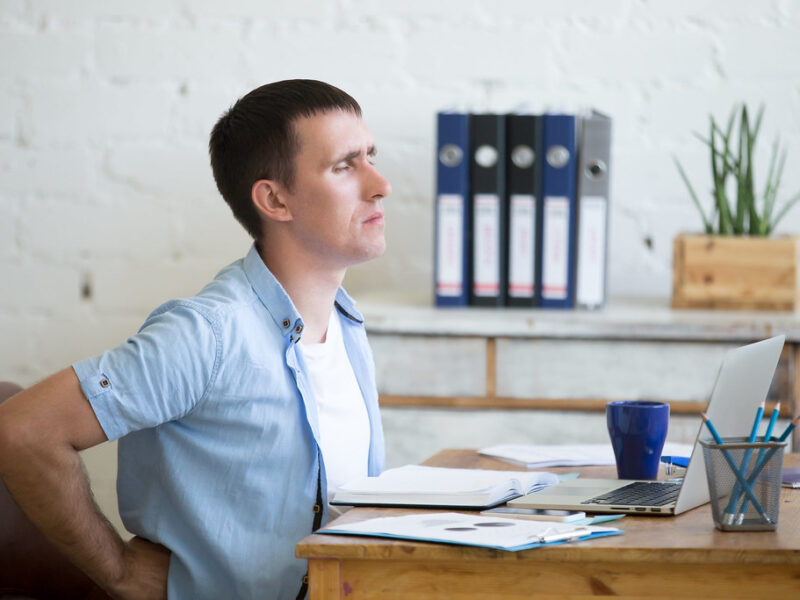Person sitting at an office desk holding their lower back
